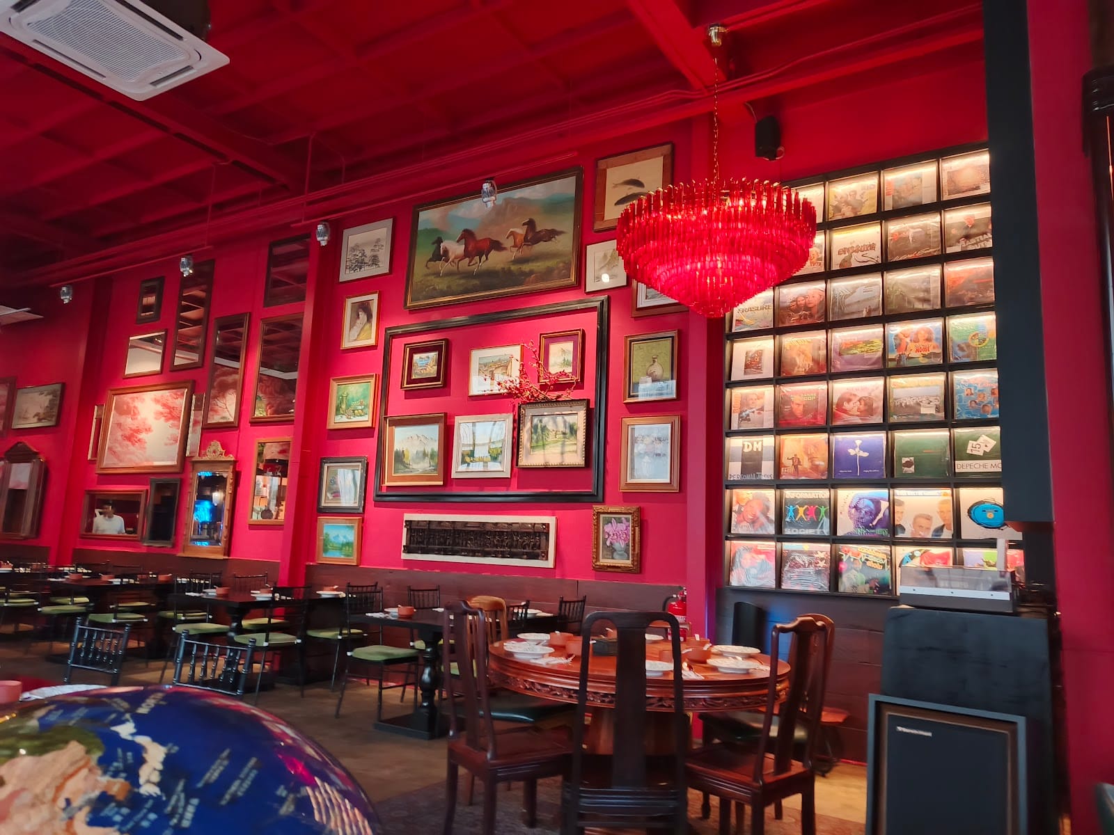 Mount Austin dining room with red walls hung with picture frames, a wall of vinyl records, a red crystal chandelier and round wooden tables
