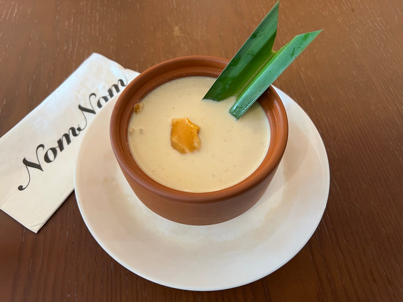 A creamy dessert in a clay bowl beside a NomNom napkin at Pelangi