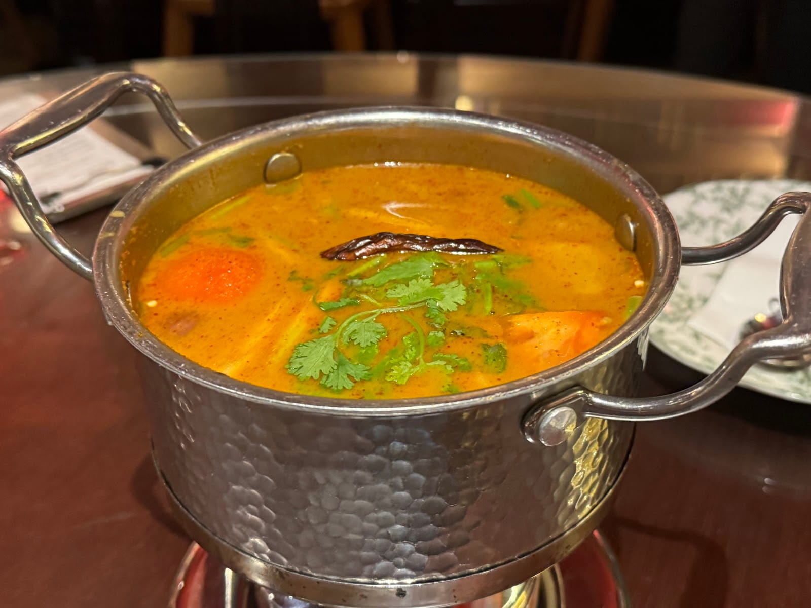Soup in a hammered steel pot with tomato, a dried chilli and coriander, served at Mount Austin
