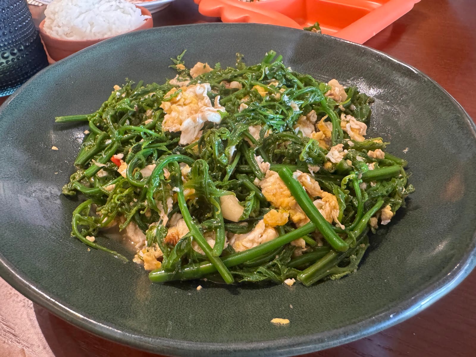 Stir-fried paku pakis fern shoots with egg in a dark green bowl at Pelangi