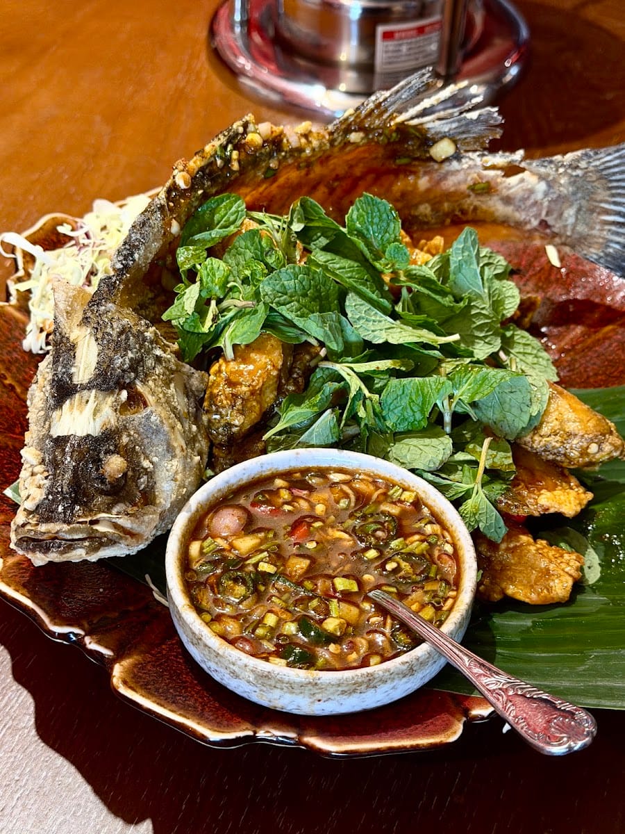 Whole fried fish on a banana leaf with a heap of fresh mint and a bowl of dipping sauce, served at Pelangi